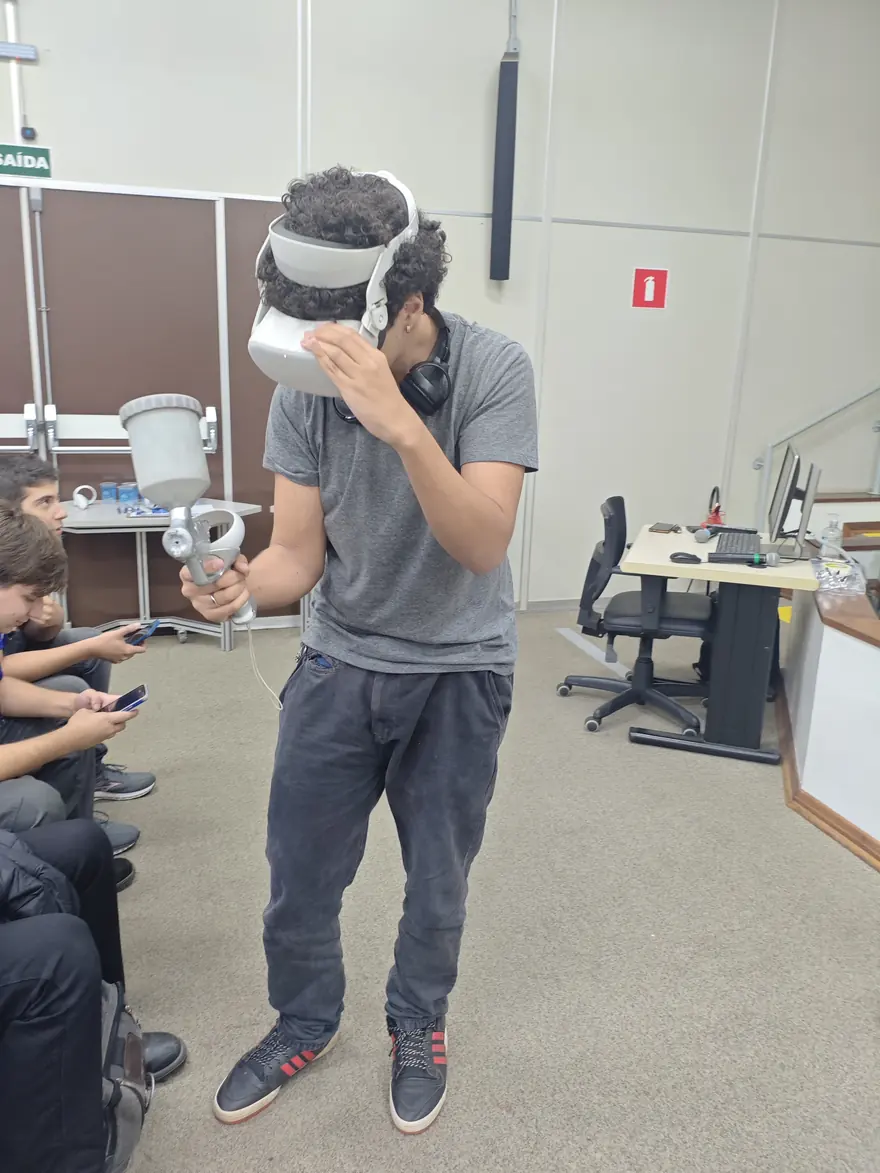 Participante com óculos de realidade virtual segurando uma pistola física de pintura durante a demonstração do curso.